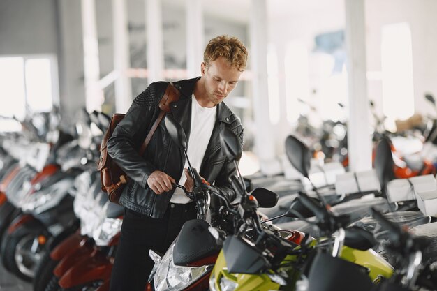 L'uomo ha scelto le motociclette nel negozio di moto. Ragazzo con una giacca nera.