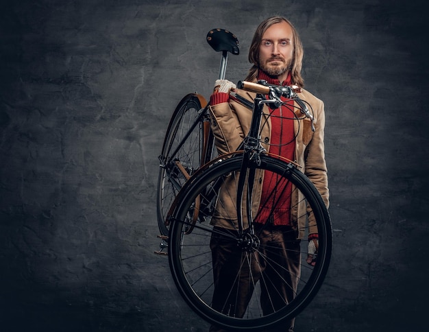 L'uomo hipster con lunghi capelli biondi tiene una bicicletta a velocità singola sulla spalla.