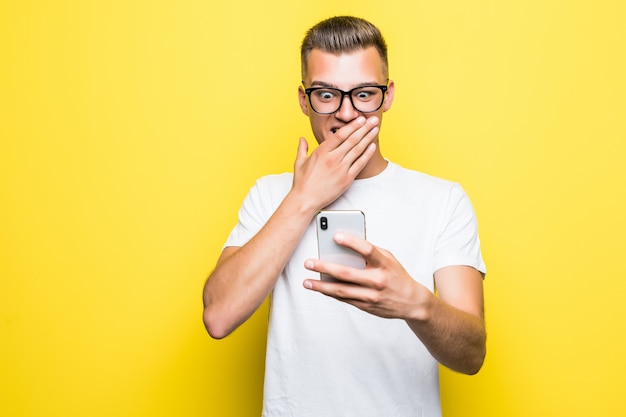 L'uomo in maglietta bianca e occhiali fa qualcosa sul suo telefono e scatta foto selfie isolate su giallo