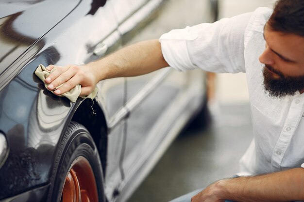 L'uomo in una camicia bianca pulisce un'auto in un autolavaggio