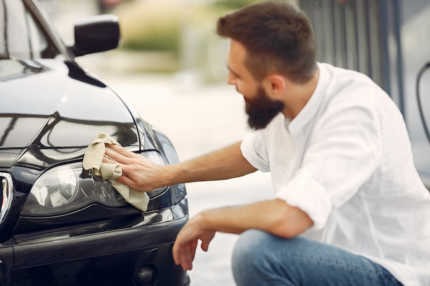 L'uomo in una camicia bianca pulisce un'auto in un autolavaggio