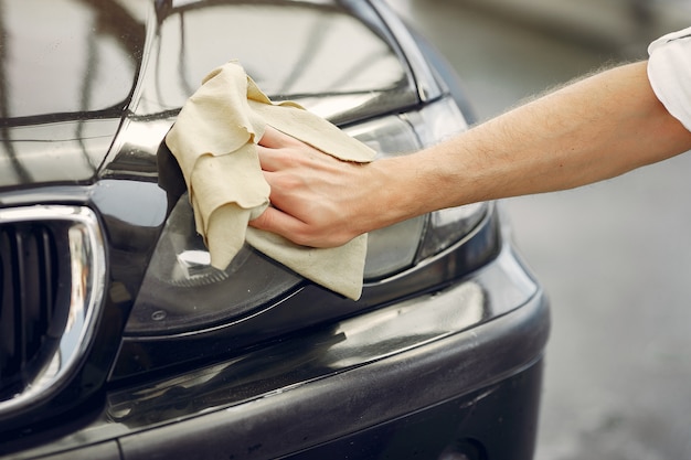 L'uomo in una camicia bianca pulisce un'auto in un autolavaggio