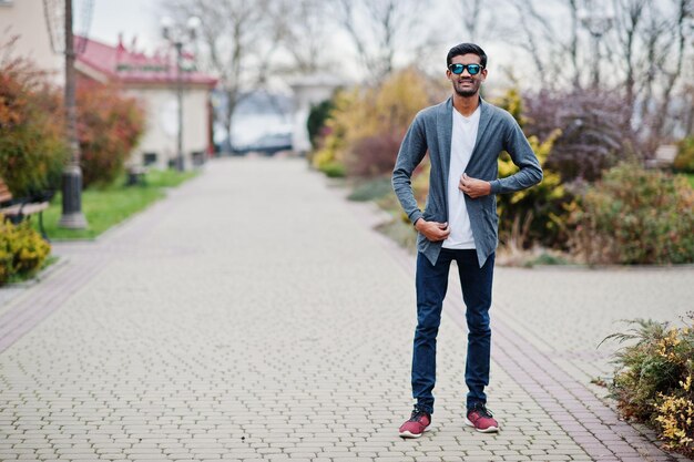 L'uomo indiano alla moda con gli occhiali da sole indossa una posa casual all'aperto