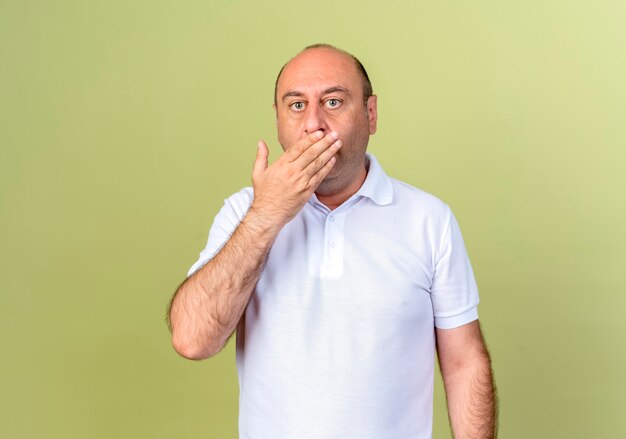 L'uomo maturo sorpreso ha coperto la bocca con la mano isolata sulla parete verde oliva