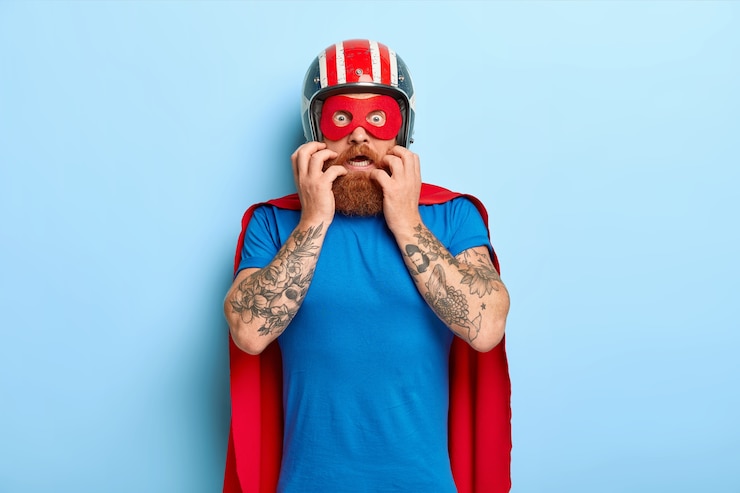 Foto gratuito l'uomo nervoso spaventato guarda con paura, indossa casco, maschera rossa e mantello, si prepara per il volo