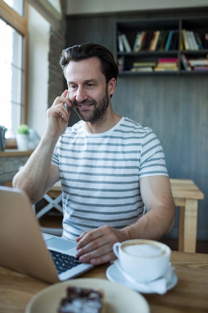 L&#39;uomo parla al telefono cellulare e con laptop in caffetteria