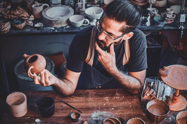 L'uomo scettico laborioso sta guardando il proprio lavoro, teiera in ceramica.