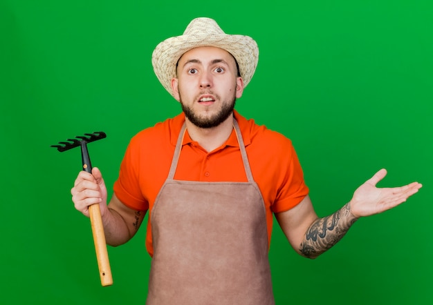 L'uomo scioccato del giardiniere che indossa il cappello da giardinaggio tiene il rastrello