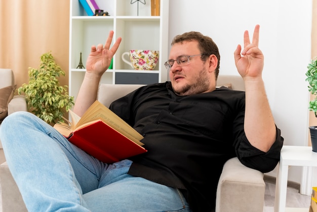 L'uomo slavo adulto sicuro in vetri ottici si siede sul libro di lettura della poltrona