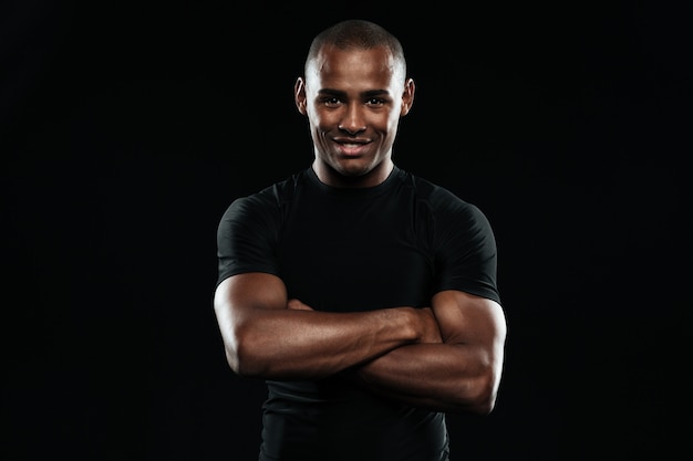 L'uomo sorridente degli sport dell'afroamericano con le braccia ha piegato l'esame della macchina fotografica