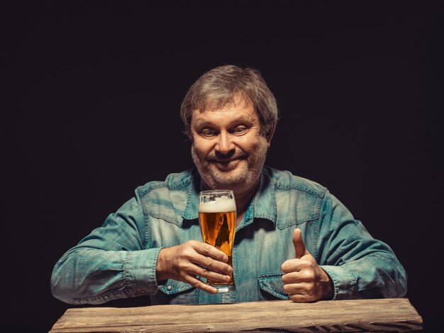 L'uomo sorridente in camicia di jeans con un bicchiere di birra