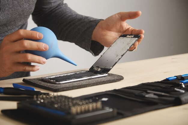 L'uomo sta lavorando con attenzione nel suo laboratorio per riparare e pulire lo smart phone utilizzando una siringa per soffiare via tutta la polvere dal dispositivo