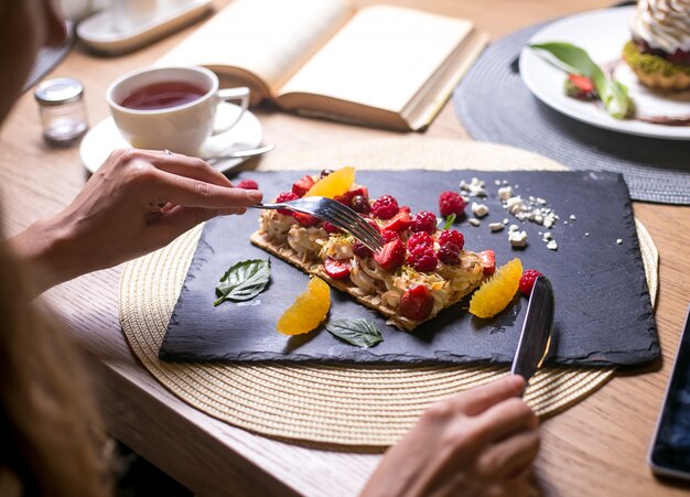 L'uomo sta per mangiare la crostata di napoleone con la vista laterale della menta dei marshmallows della ciliegia dell'arancia del lampone della crema