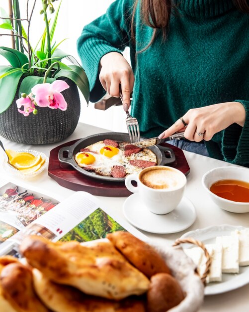 L'uomo taglia l'uovo con la vista laterale del limone del pane del caffè delle salsiccie