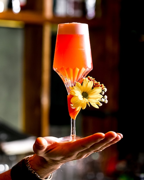 L'uomo tiene un bicchiere di cocktail arancione guarnito con fiori