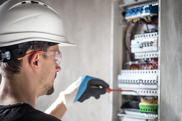 L'uomo, un tecnico elettrico che lavora in un quadro elettrico con fusibili. Installazione e collegamento di apparecchiature elettriche.