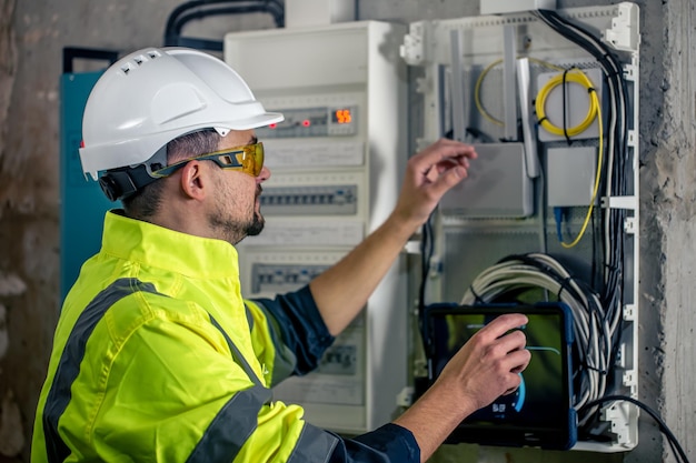 L'uomo un tecnico elettrico che lavora in un quadro elettrico con fusibili utilizza un tablet