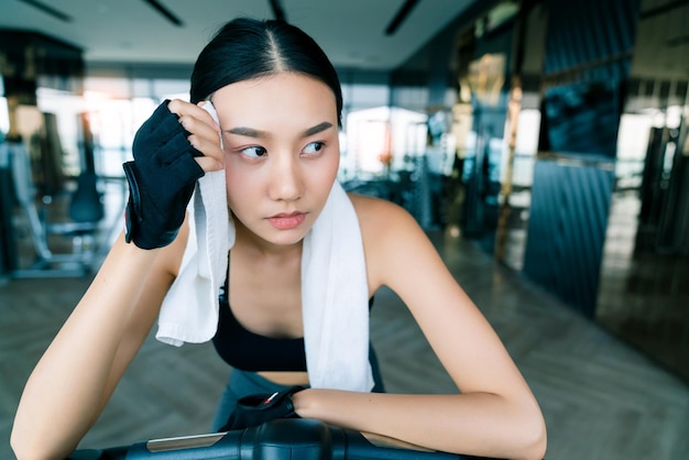 L'usura sportiva della donna asiatica forte e ferma si rilassa sulla priorità bassa bianca di forma fisica del tovagliolo della tenuta della mano della bicicletta