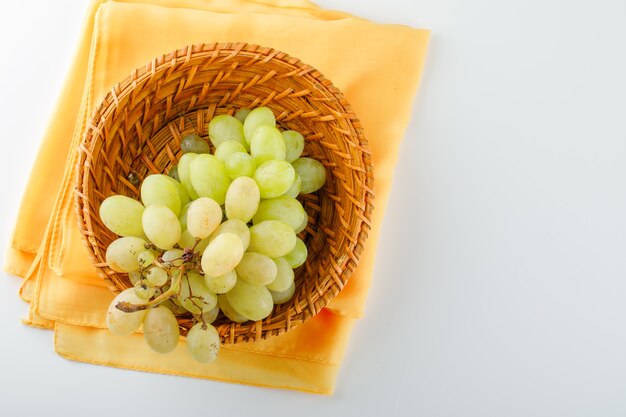 L'uva verde in un cesto di vimini piatto giaceva su bianco e tessuto