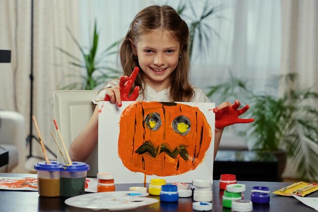 La bambina carina tiene un poster con la zucca di Halloween dipinta.