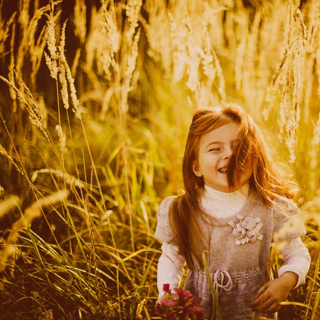 La bambina con capelli rossi si leva in piedi sul campo di autunno