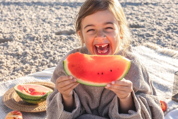 La bambina del primo piano mangia l'anguria sulla spiaggia