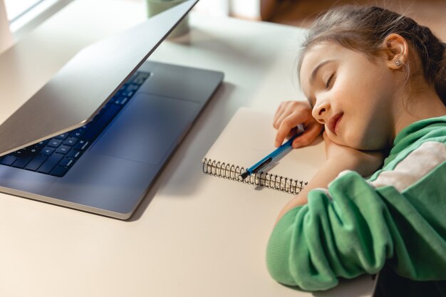 La bambina dorme davanti a un computer portatile sul tavolo