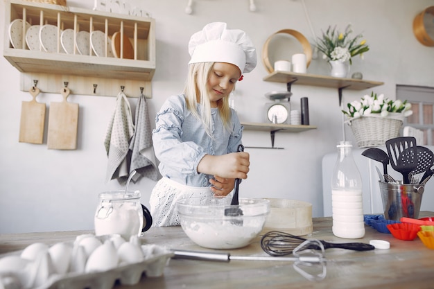 La bambina in un cappello bianco dello shef cucina l'impasto per i biscotti