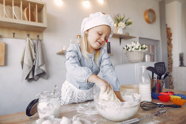 La bambina in un cappello bianco dello shef cucina l'impasto per i biscotti