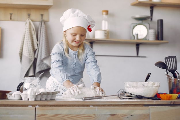 La bambina in un cappello bianco dello shef cucina l'impasto per i biscotti