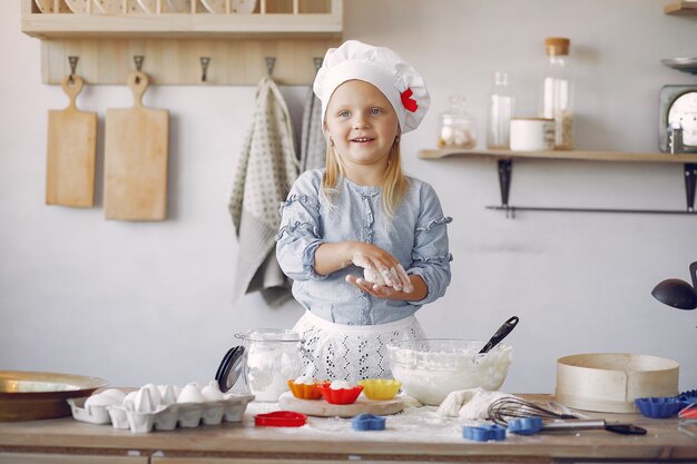 La bambina in un cappello bianco dello shef cucina l'impasto per i biscotti