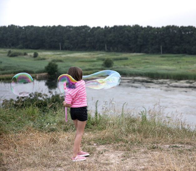 La bambina lancia enormi bolle di sapone sullo sfondo della bellissima natura.