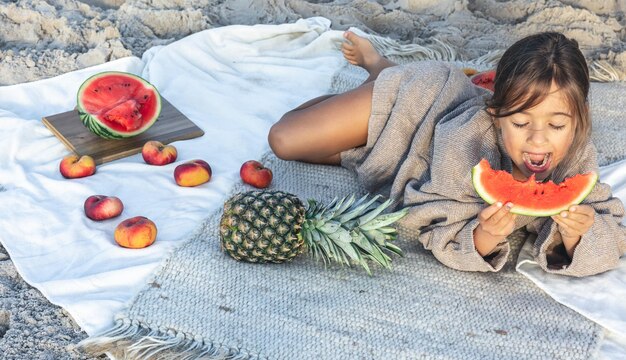 La bambina mangia la frutta sdraiata su una coperta sulla spiaggia