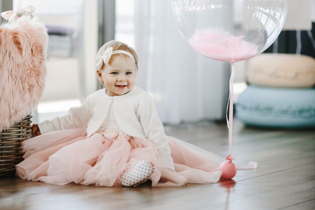 La bambina sorridente in un affascinante vestito rosa si siede sul pavimento