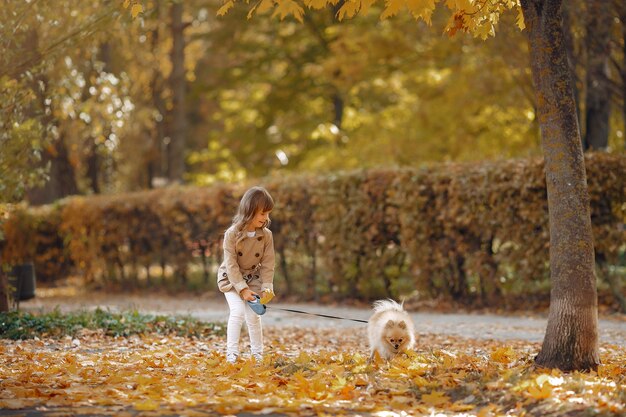 La bambina sveglia cammina in un parco di autunno con un cane