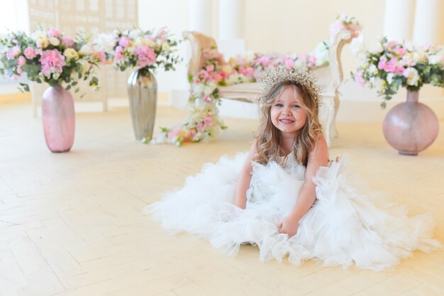 La bambina vestita come una principessa si siede tra i fiori nella stanza