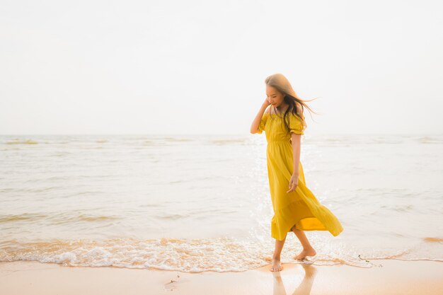 La bella camminata asiatica della giovane donna del ritratto sull&#39;oceano del mare e della spiaggia con il sorriso felice si distende