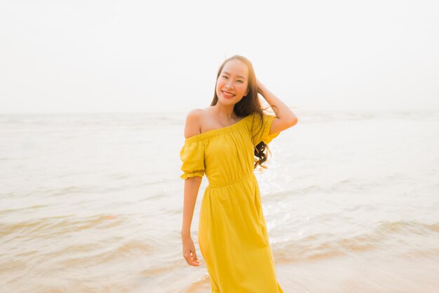 La bella camminata asiatica della giovane donna del ritratto sull&#39;oceano del mare e della spiaggia con il sorriso felice si distende