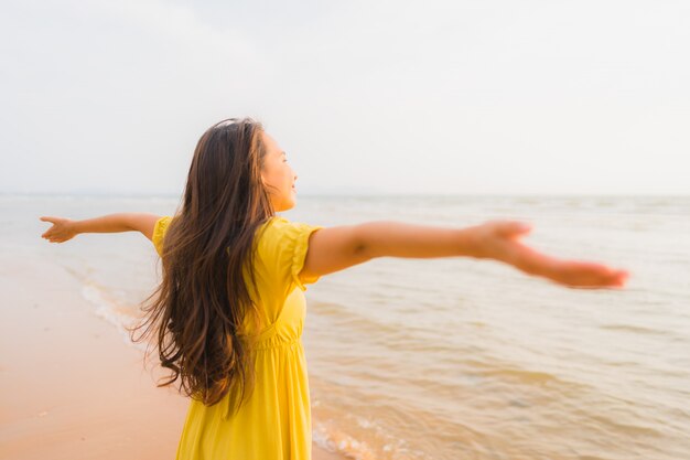 La bella camminata asiatica della giovane donna del ritratto sull&#39;oceano del mare e della spiaggia con il sorriso felice si distende