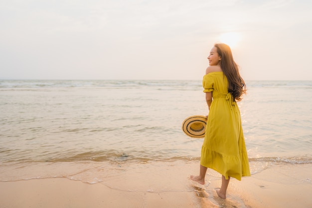 La bella camminata asiatica della giovane donna del ritratto sull&#39;oceano del mare e della spiaggia con il sorriso felice si distende