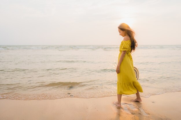 La bella camminata asiatica della giovane donna del ritratto sull&#39;oceano del mare e della spiaggia con il sorriso felice si distende