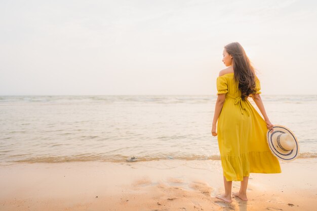 La bella camminata asiatica della giovane donna del ritratto sull&#39;oceano del mare e della spiaggia con il sorriso felice si distende