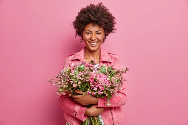 la bella donna afroamericana esprime emozioni sincere, abbraccia bouquet di fiori, ha umore primaverile