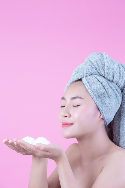 La bella donna Asia sta lavando il suo fronte su fondo rosa.