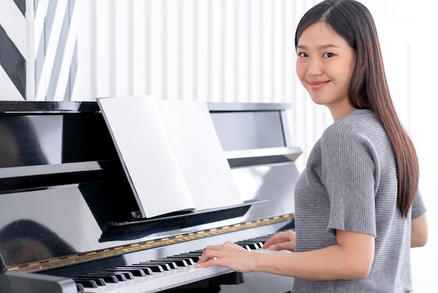 La bella donna asiatica casual si diverte a praticare il pianoforte si rilassa e lo sfondo della casa di felicità