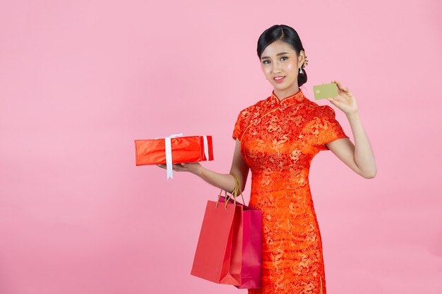 La bella donna asiatica sorride felice e mostra la carta di credito nel nuovo anno cinese su sfondo rosa.