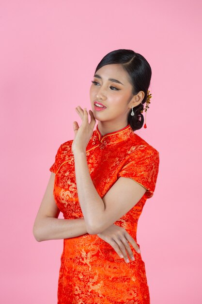 La bella donna asiatica sorride felice e ti mostra qualcosa nel nuovo anno cinese su sfondo rosa.