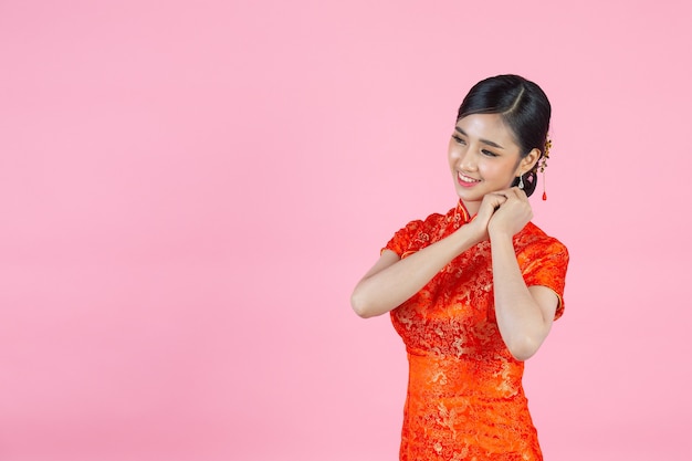 La bella donna asiatica sorride felice e ti mostra qualcosa nel nuovo anno cinese su sfondo rosa.
