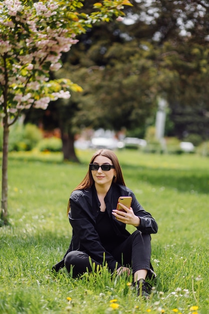 La bella donna castana allegra di buon umore usa il telefono esterno