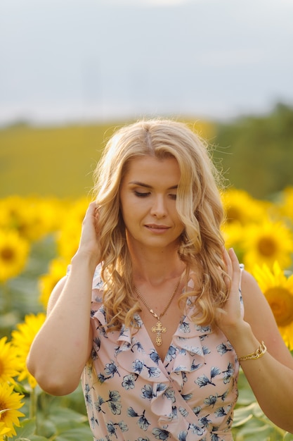 La bella donna posa nel campo agricolo con il girasole un giorno di estate soleggiato